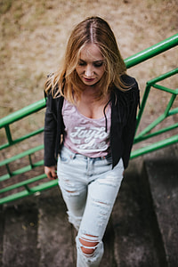 Blonde woman in a black jacket and ripped jeans by a green handrail thumbnail