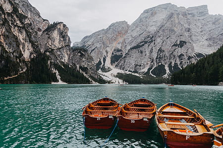 three brown wooden boats on body of water surrounded by mountains thumbnail