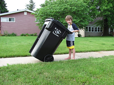 boy holding black trash bin near house thumbnail