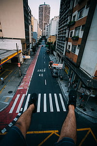 Person Wearing Black Lace Up Sneakers Facing Gray Concrete Road Top Between Concrete Buldings thumbnail