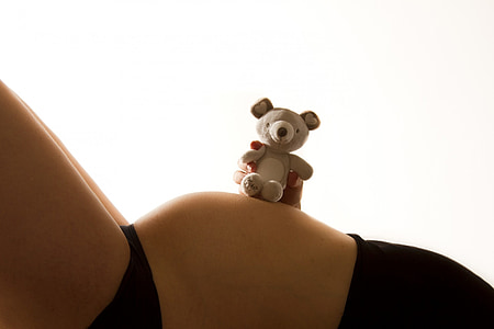 woman holding grey teddy bear on top of her belly thumbnail