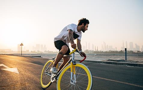 man wearing crew-neck shirt and black shorts riding on yellow and gray bike thumbnail