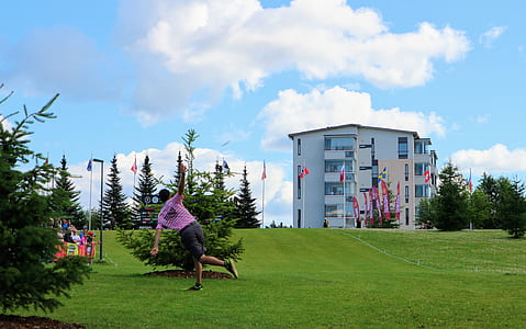 man standing with one leg while hands wide spreading on green grass field with white concrete building ahead during daytime thumbnail