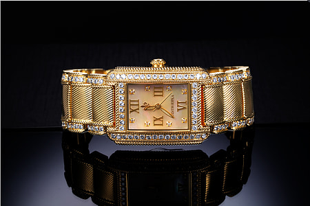 rectangular gold-colored analog watch on glass surface displaying 12:36 thumbnail