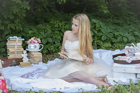 woman in white dress holding notebook while sitting on white textile during daytime thumbnail