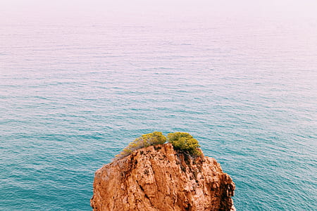 brown rock formation surrounded by water thumbnail