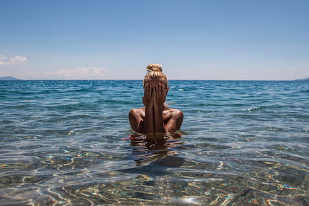 woman in body of water covering its face with hand under blue skies thumbnail