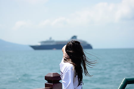 woman standing and leaning on brown railing beside body of water and ship at daytime thumbnail