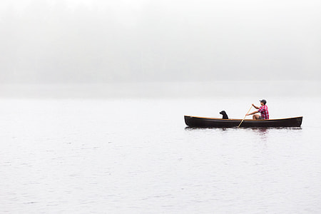 man and dog riding canoe on body of water thumbnail