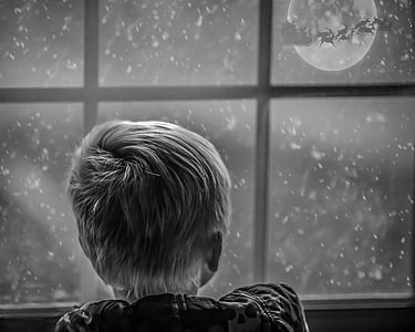 grayscale photo of boy leaning on window looking at moon during nighttime thumbnail