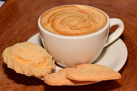 latte in ceramic teacup with three pastries on white ceramic saucer on brown wooden surface thumbnail