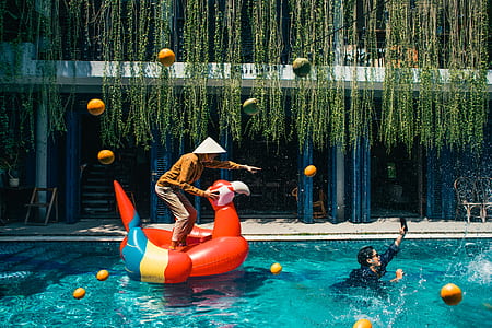 man standing on inflatable scarlet macaw in pool thumbnail