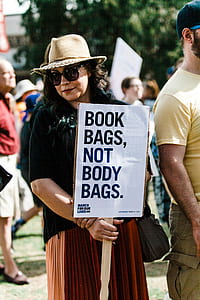 woman standing while holding book bags, not body bags. sign at daytime thumbnail