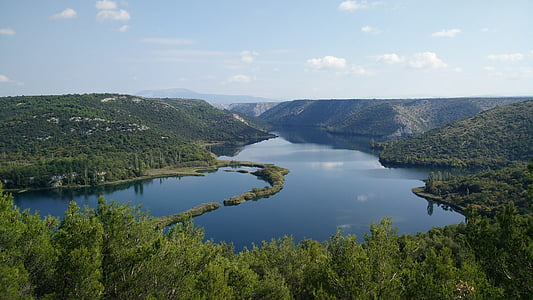 calm body of water surrounded by mountains and trees thumbnail