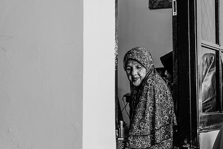 grayscale photography of a woman standing near doorway thumbnail