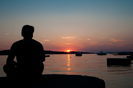 silhouette of man sitting on rock near body of water thumbnail