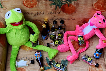 Kermitt the frog and Pink Panther plush toys on brown sofa with bottles thumbnail