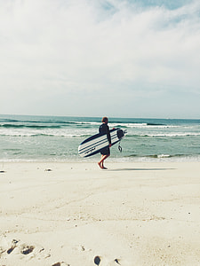 man carrying white and blue surfboard walking on the seashore thumbnail
