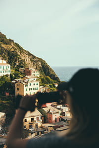 woman taking photo of concrete houses near mountains thumbnail