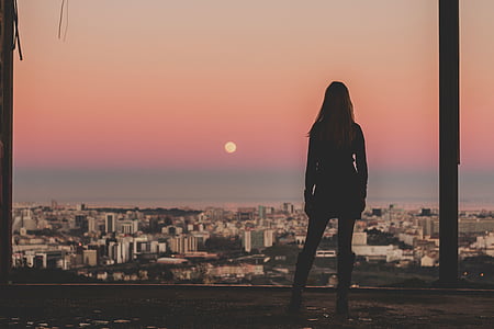 silhouette of woman standing front of buildings during golden hour thumbnail