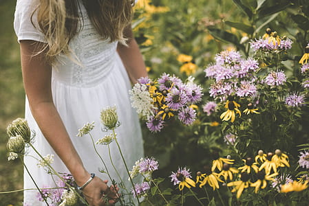 woman wearing white short-sleeved dress infront of flower bed outdoors thumbnail