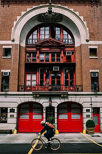 person riding on bike beside brown building thumbnail