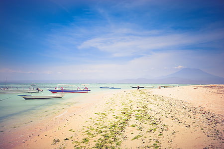 person walking at the seashore near wooden boats under blue sky thumbnail