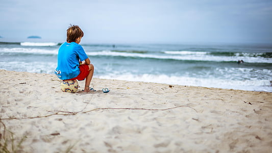 boy sitting on soccer ball in front ocean at daytime thumbnail
