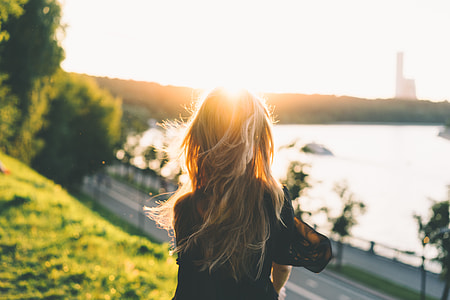 blonde person in black jacket back view in front of ocean and building thumbnail