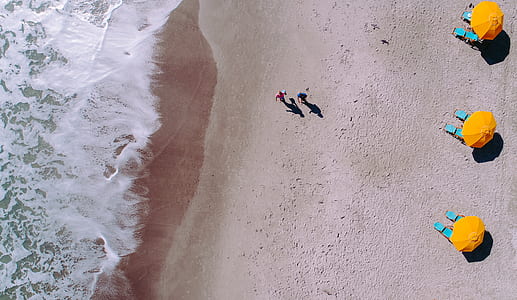 aerial photography of two person walking near seashore at daytime thumbnail
