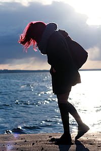 woman walking on sand ground near body of water during daytime thumbnail