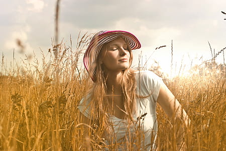 Young woman in striped hat sitting and posing in a wheat field with eyes closed thumbnail