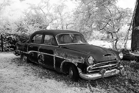 grayscale photography of wrecked sedan near trees thumbnail