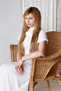 blonde woman wearing white dress sitting on brown wicker chair thumbnail