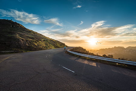 person standing beside road guard rail near green mountain at golden hour thumbnail
