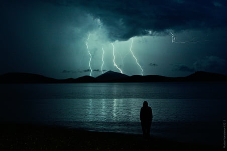 person standing near seashore and mountain cliff with thunder thumbnail