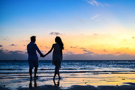 Man and Woman Holding Hands Walking on Seashore during Sunrise thumbnail