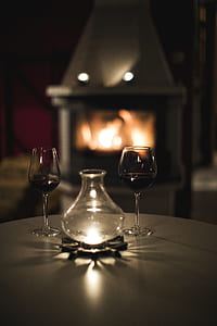 clear glass votive candle bottle between of two clear wine glasses on table lowlight photography thumbnail