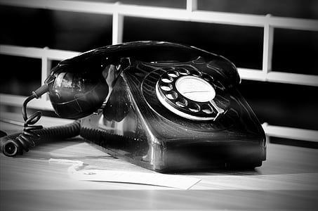 grayscale photography of rotary telephone near white metal window grille thumbnail