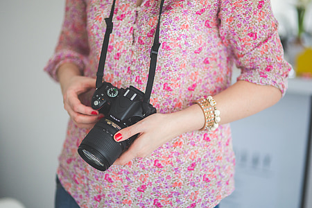 person wearing red floral shirt holding black DSLR camera thumbnail