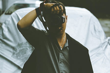 man standing in front of vehicle while holding black Canon DSLR camera thumbnail