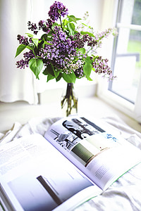 purple lilacs in clear glass bottle beside opened book thumbnail
