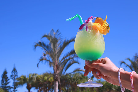 person holding yellow and teal liquid filled footed glass under clear blue sky thumbnail