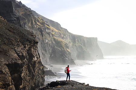 man standing on gray rock near body of water during daytime thumbnail
