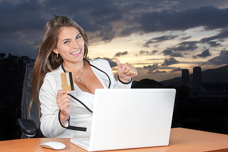 woman wearing white blazer using MacBook White with credit card on her right hand outdoors thumbnail