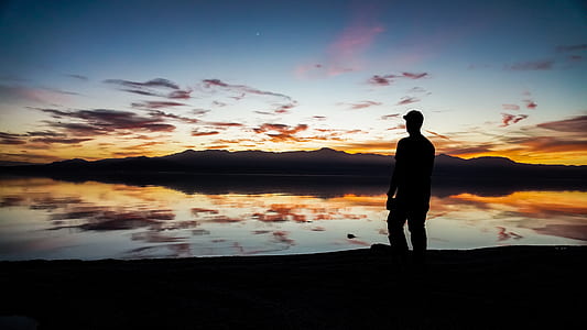 silhouette photo of man standing near body of water thumbnail