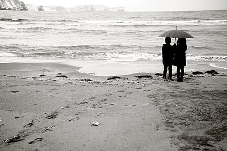 gray scale photo of two girls holding gray umbrella standing beside body of water thumbnail