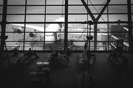 grayscale photo of people sitting on airport waiting bench thumbnail