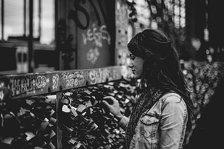 grayscale photography of standing woman front of brown wooden fence thumbnail