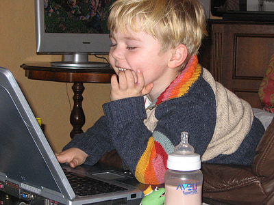 smiling blonde haired boy using laptop computer beside brown table thumbnail